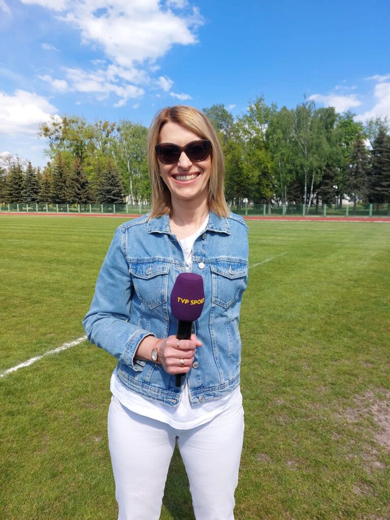 Paulina Malinowska-Kowalczyk na boisku piłkarskim z mikrofonem TVP Sport w ręce.
