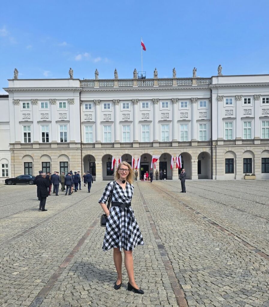 Paulina Malinowska-Kowalczyk w czarno białej sukience na tle Pałacu Prezydenckiego