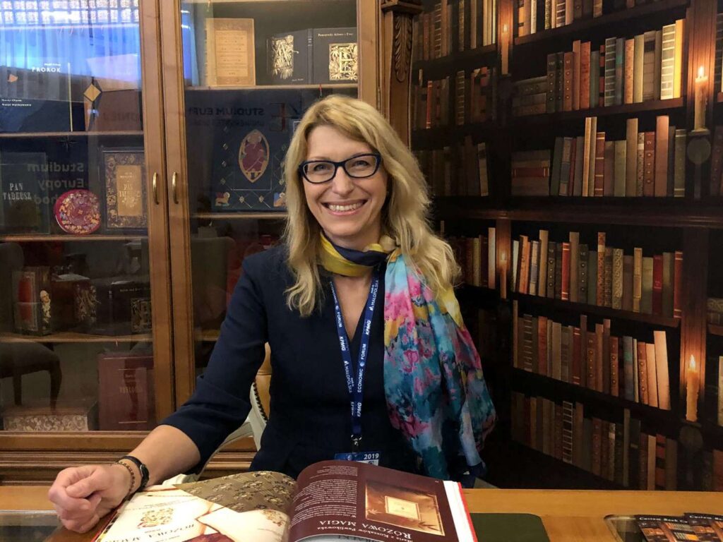 Paulina Malinowska-Kowalczyk siedzi przy biurku na tle biblioteki.